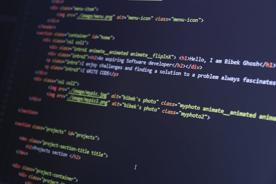 A close-up image of a person's hand operating a laptop computer on a wooden surface, with visible code displayed on the screen. The individual is wearing a black wristwatch, and the scene is lit with 